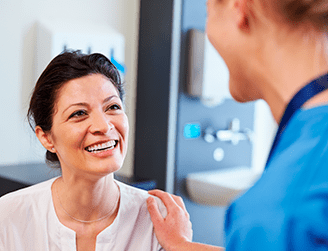 Paciente mulher sorrindo sendo acolhida por profissional de medicina. Programa de apoio ao paciente crônico gerencia a saúde de pacientes com determinadas doenças crônicas e os auxilia nos tratamentos em geral e em eventuais complicações. Fornece orientações, esclarecimentos e suporte emocional por telefone.