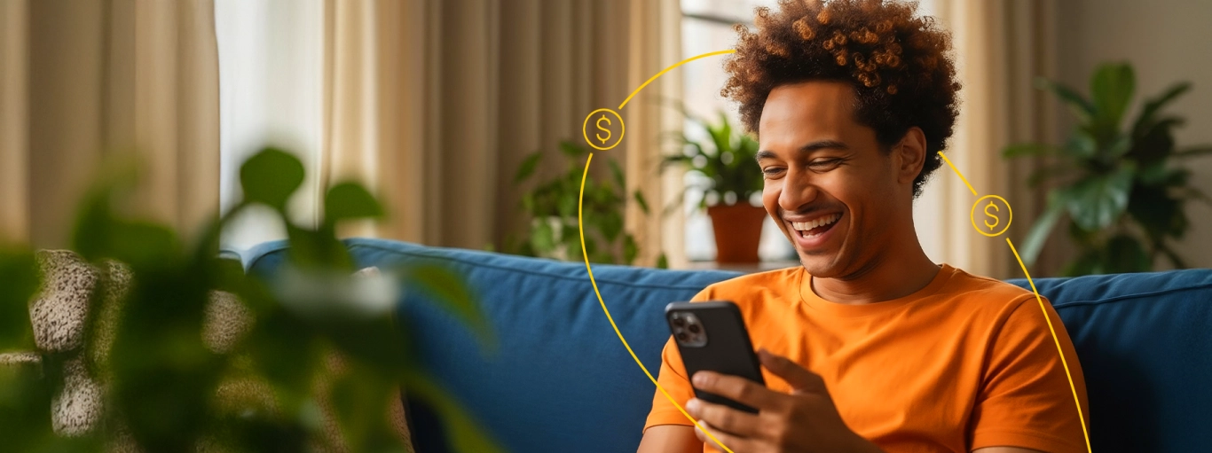 Homem sentado no sofá olhando para o celular e sorrindo.