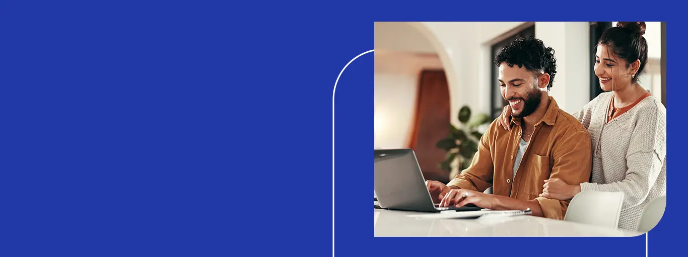 Duas pessoas em casa, sorrindo e colaborando, usam um notebook em um ambiente claro e acolhedor, transmitindo parceria e tranquilidade.