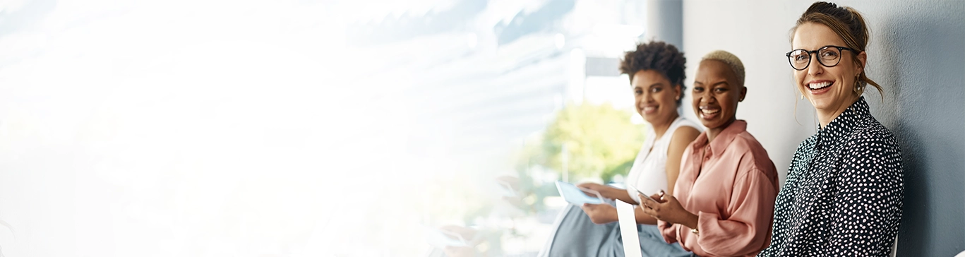 Três mulheres sorridentes sentadas em um ambiente iluminado.